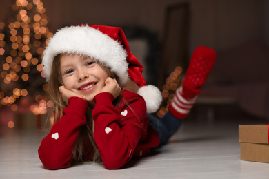 Photo of Cute little child wearing Santa hat at home. Christmas time