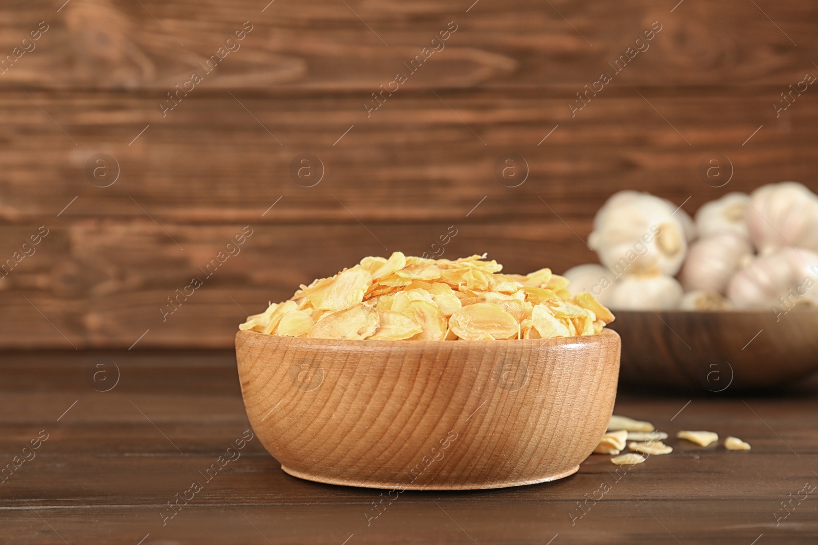 Photo of Bowl with dried garlic flakes on wooden table