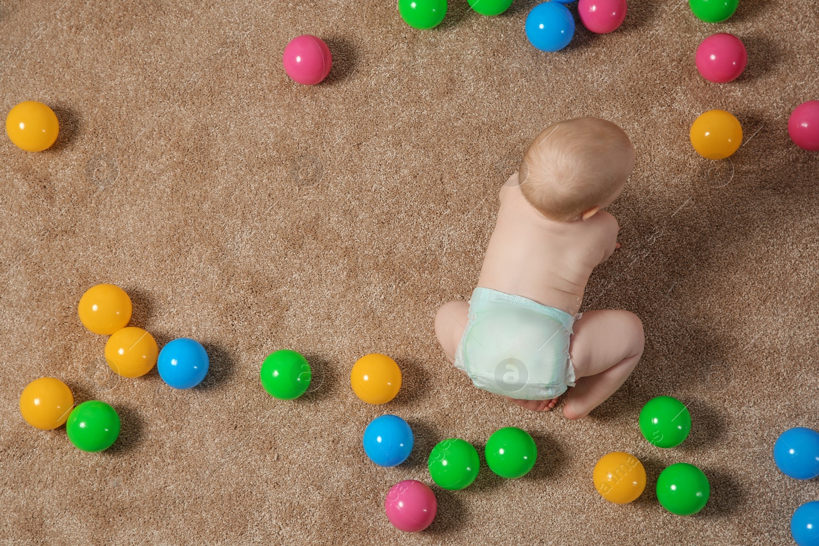Photo of Cute little baby crawling on carpet with toys, top view