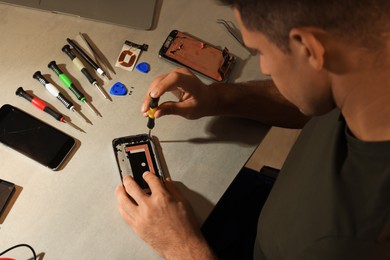 Photo of Man repairing broken smartphone at table, above view