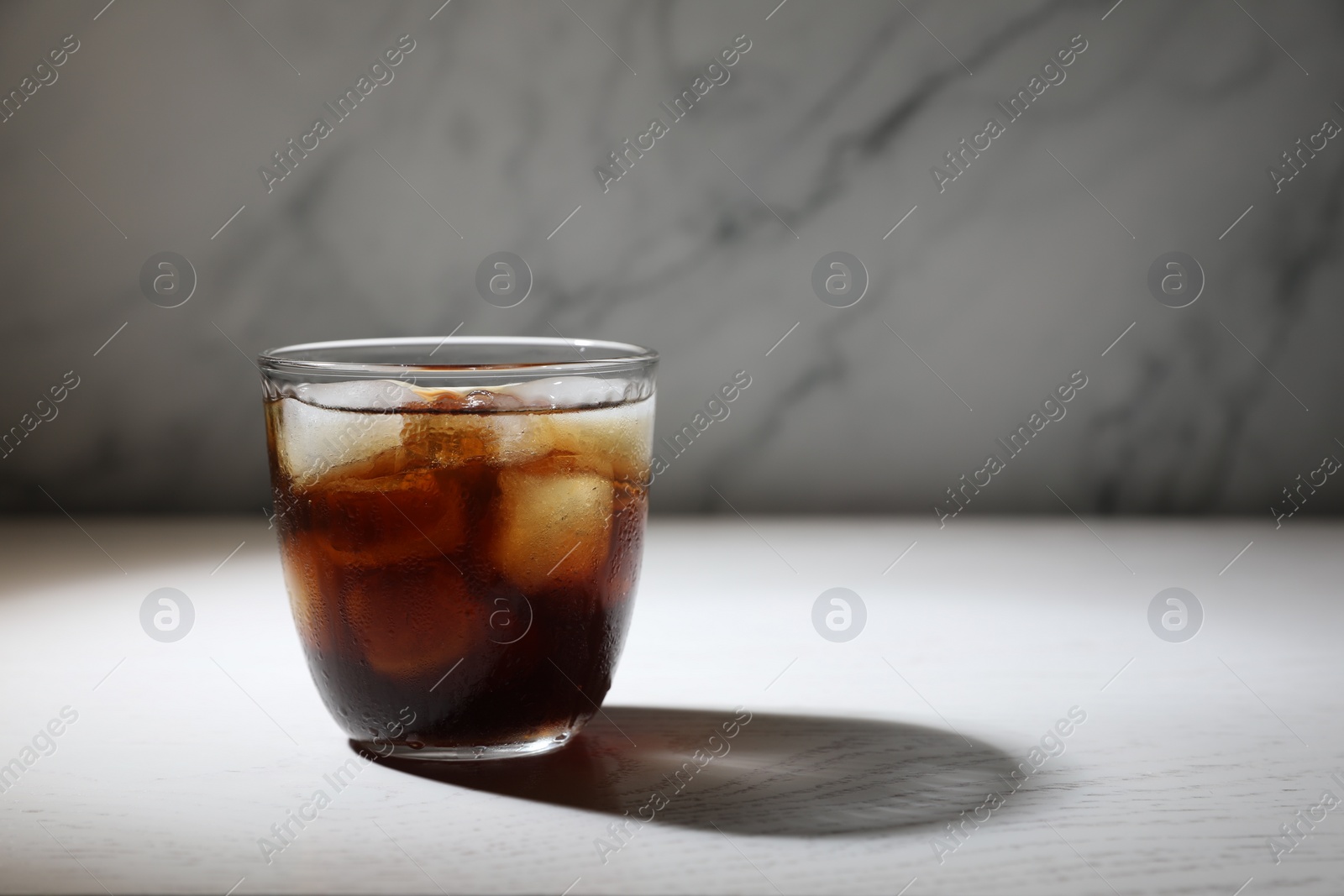 Photo of Refreshing iced coffee in glass on white wooden table. Space for text