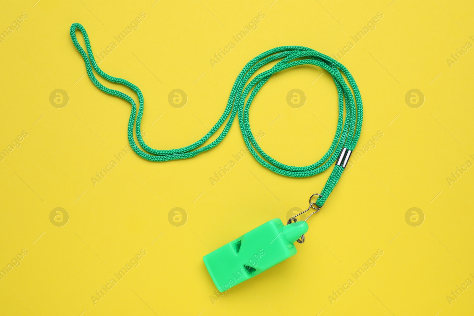 Photo of One green whistle with cord on yellow background, top view