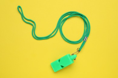 One green whistle with cord on yellow background, top view