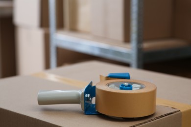 Photo of Adhesive tape dispenser on cardboard box indoors. Space for text