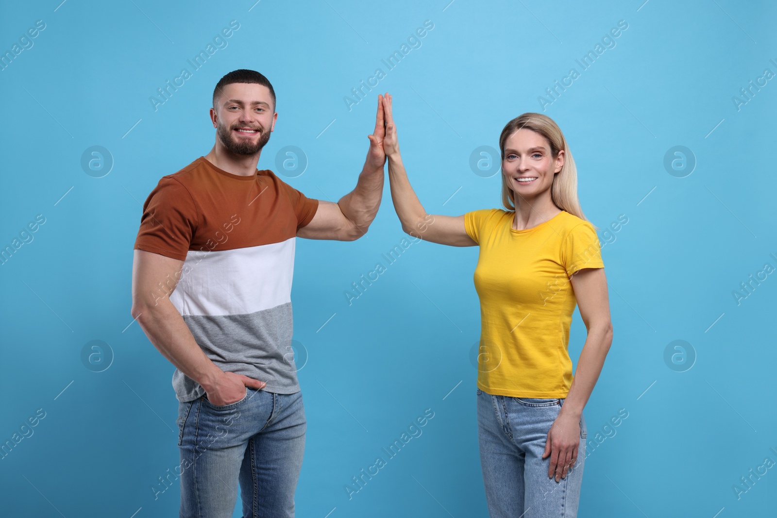 Photo of Happy couple giving high five on light blue background