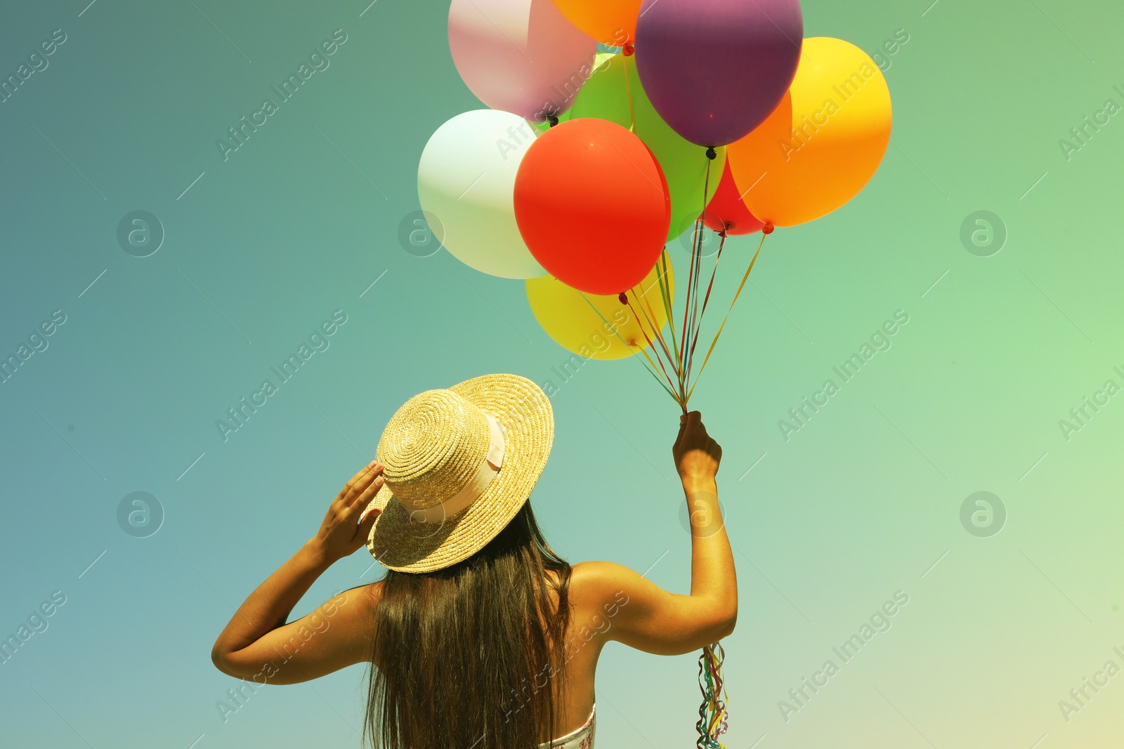 Image of Woman holding bunch of colorful balloons against sky on sunny day, back view