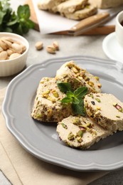 Photo of Tasty halva with pistachios and mint on table, closeup