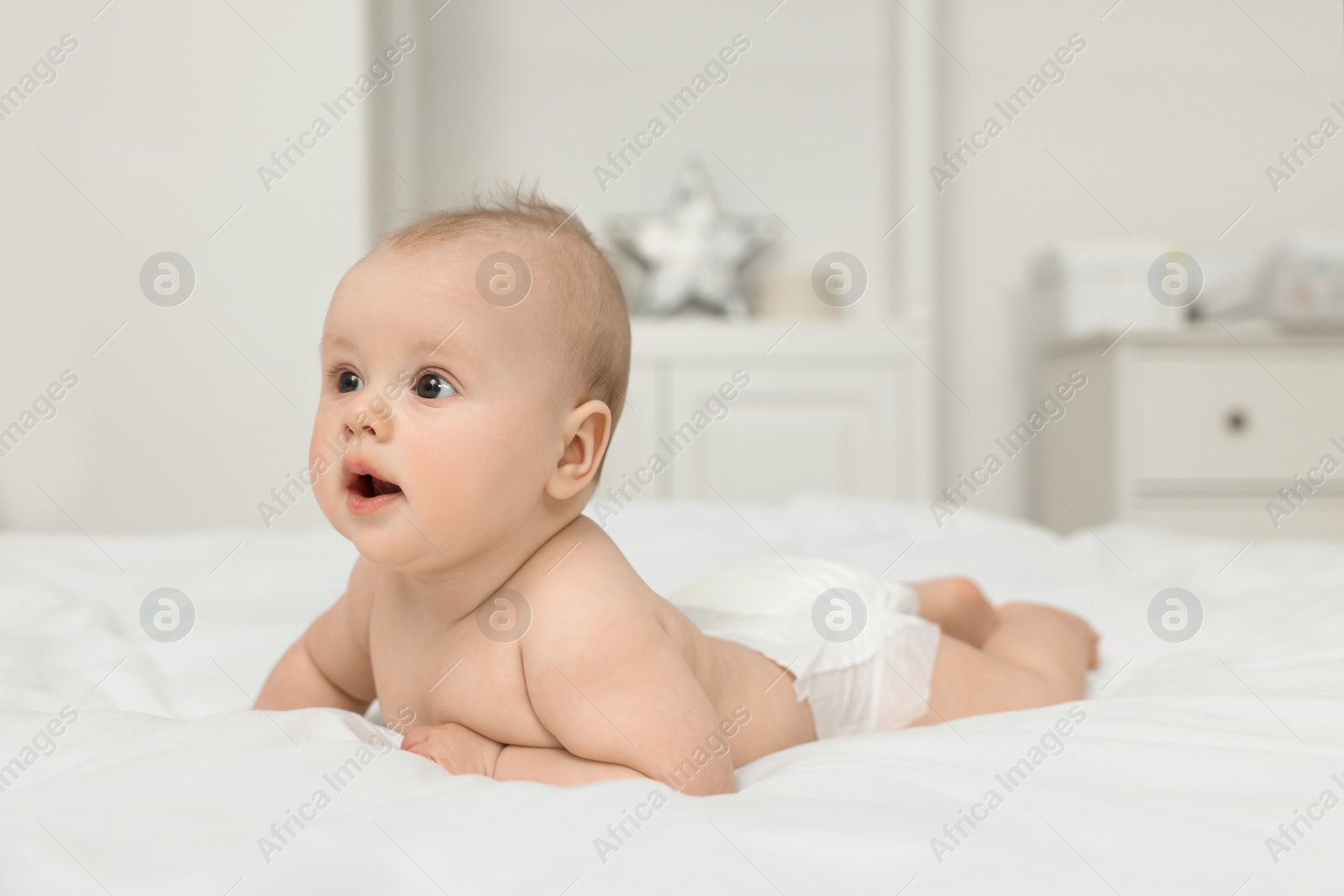 Photo of Cute baby lying on white bed at home, space for text