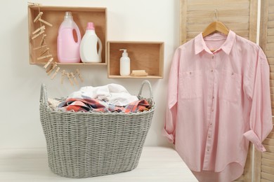 Photo of Wicker basket with dirty laundry on white table in bathroom