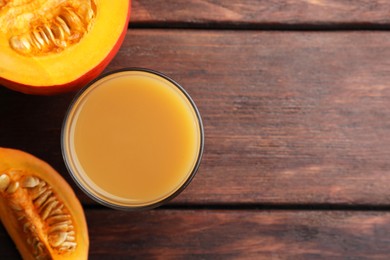 Tasty pumpkin juice in glass and cut pumpkin on wooden table, flat lay. Space for text