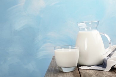 Photo of Glass and jug of fresh milk on wooden table against color background. Space for text