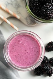 Glass of blackberry smoothie and berries on white table, flat lay