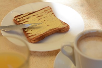 Photo of Cup of coffee and delicious sandwich with butter on beige table, closeup