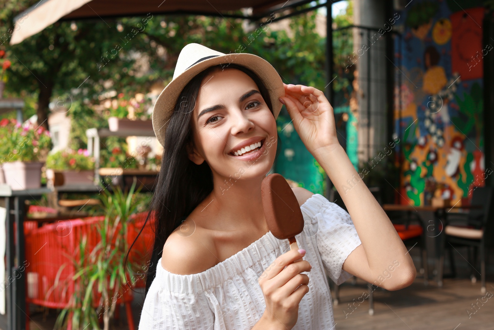 Photo of Beautiful young woman holding ice cream glazed in chocolate on city street