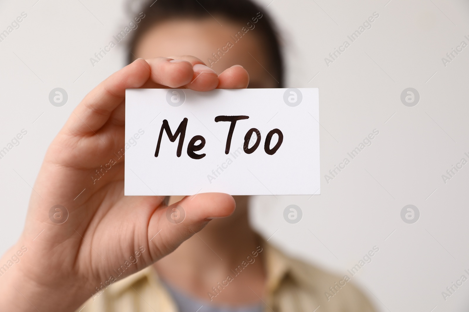 Photo of Woman holding paper with text MeToo against light background, closeup. Stop sexual assault