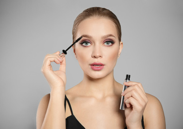 Photo of Beautiful woman applying mascara on light grey background. Stylish makeup