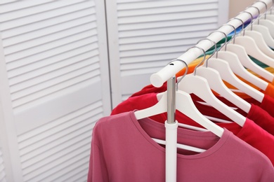 Photo of Rack with bright clothes in room. Rainbow colors