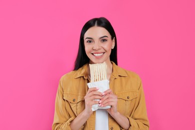 Happy young woman with delicious shawarma on pink background
