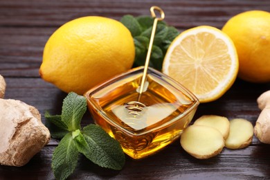 Photo of Natural cough remedies. Bowl with honey, ginger, lemon and mint on wooden table, closeup