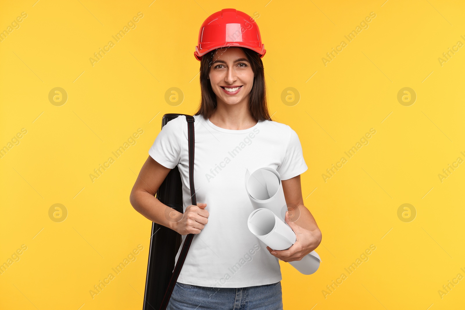 Photo of Architect in hard hat with drafts and tube on yellow background