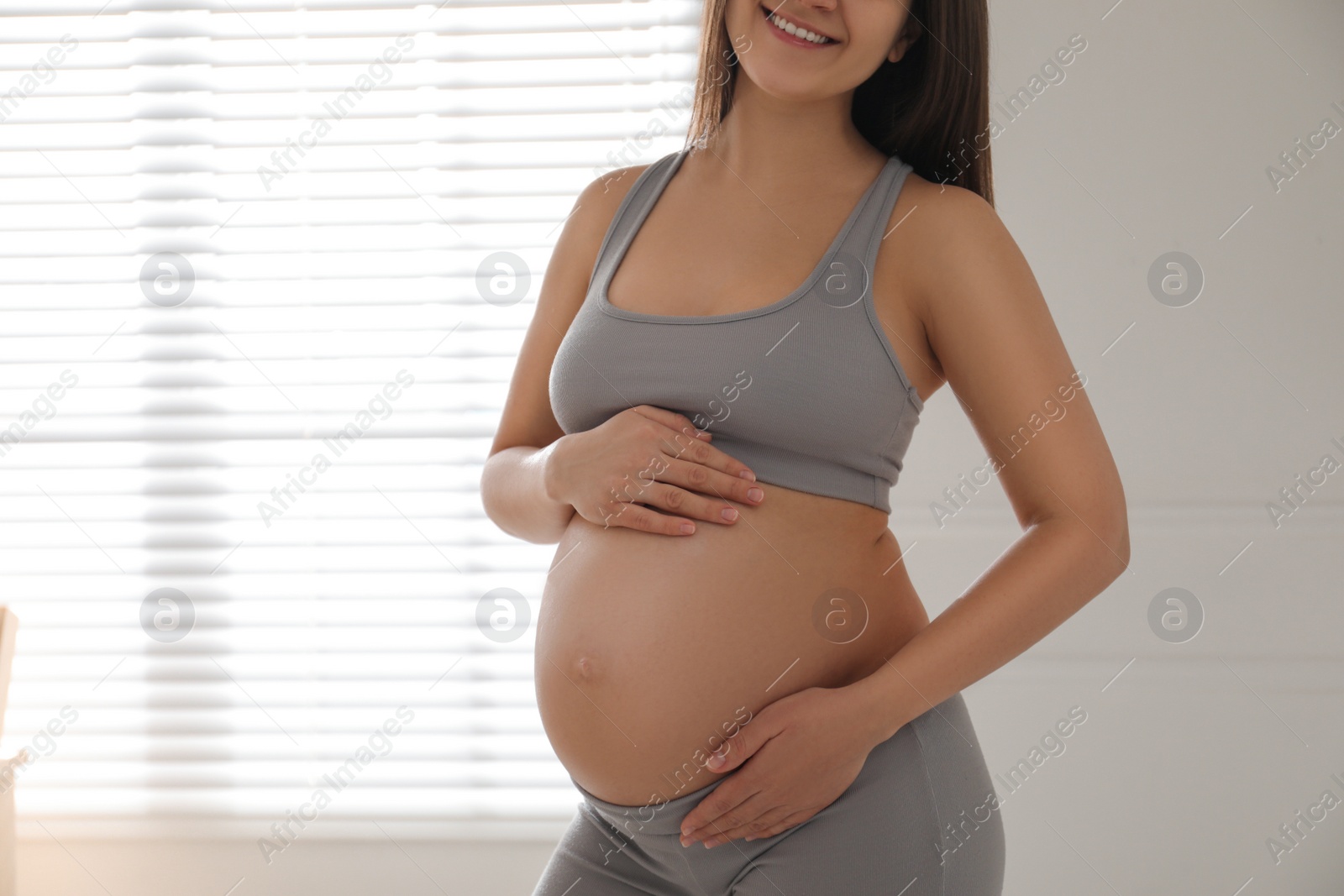 Photo of Pregnant young woman touching belly near window indoors, closeup. Space for text