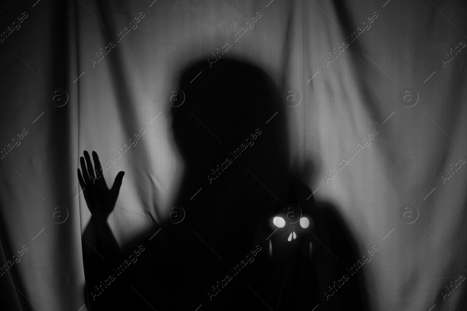 Photo of Silhouette of creepy ghost with skull behind grey cloth