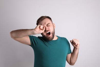 Sleepy young man yawning on light background