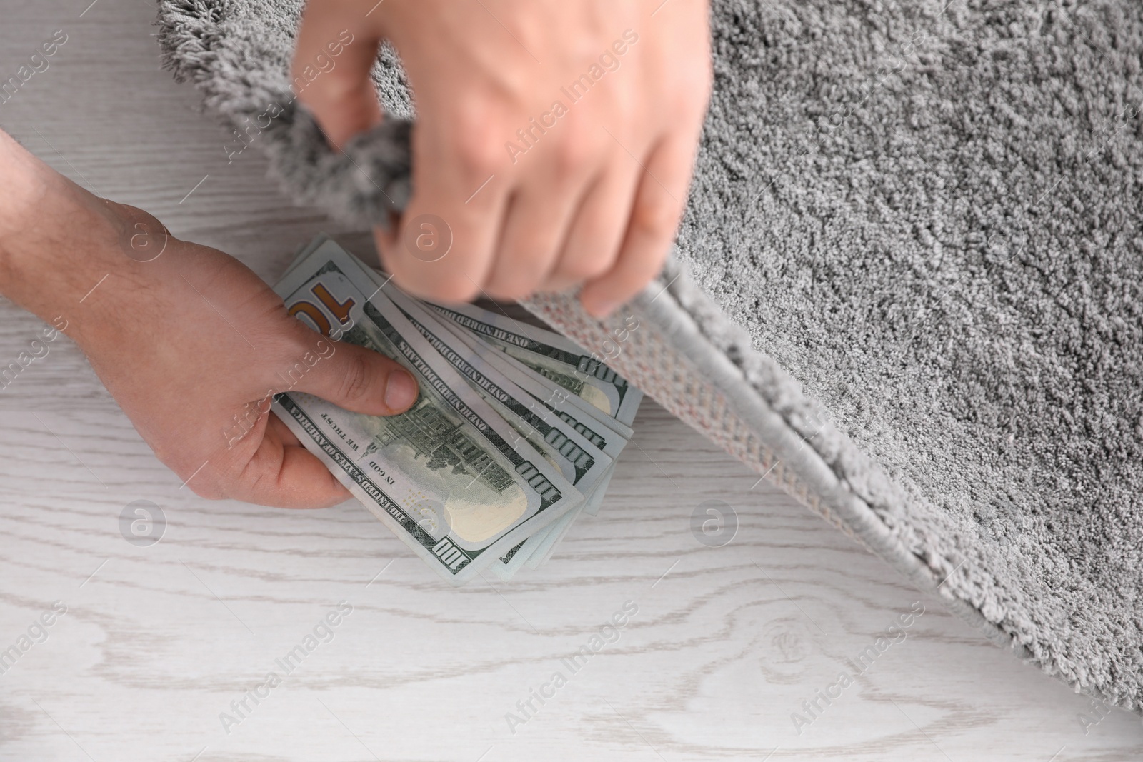 Photo of Man hiding money under carpet indoors, closeup. Financial savings