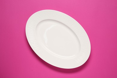 Photo of One white plate on pink background, top view