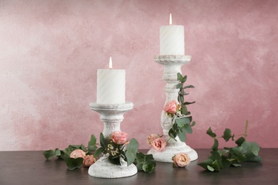 Photo of Vintage candlesticks with burning candles, roses and eucalyptus on table