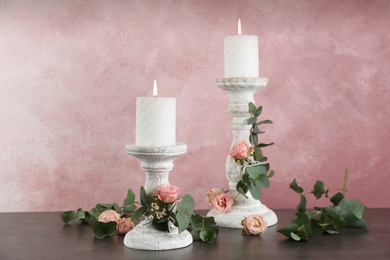 Vintage candlesticks with burning candles, roses and eucalyptus on table