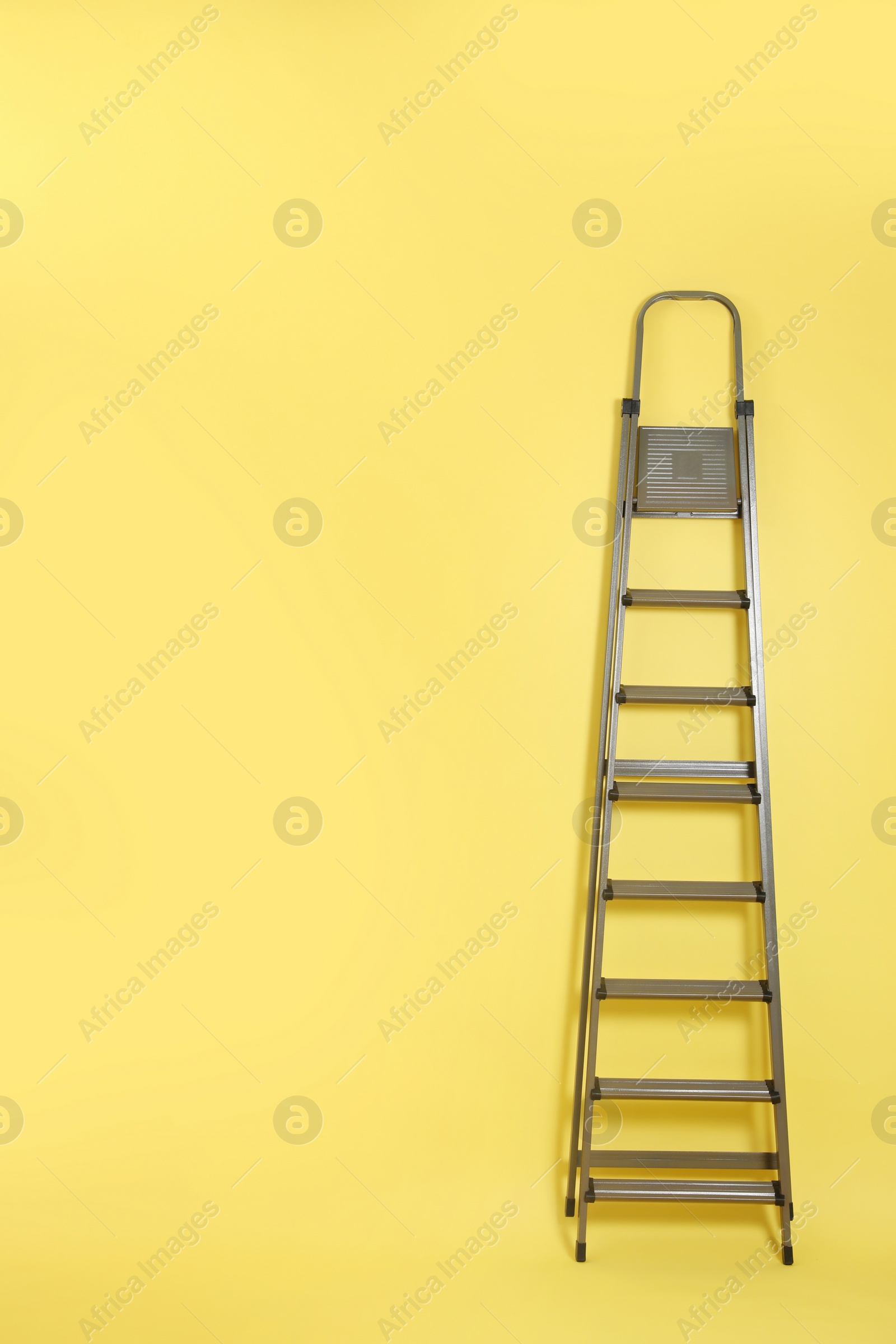 Photo of Metal stepladder on yellow background. Space for text