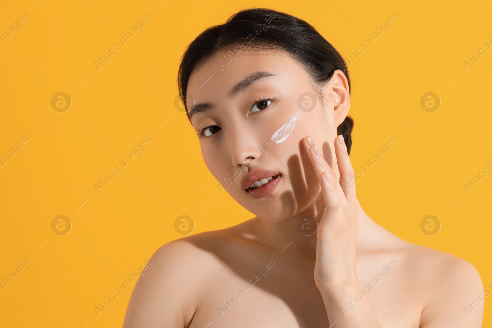 Photo of Beautiful young woman with sun protection cream on her face against orange background, space for text