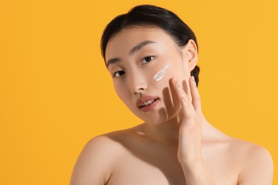 Beautiful young woman with sun protection cream on her face against orange background, space for text