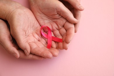 Photo of Senior woman and her adult daughter holding pink ribbon on color background, top view. Breast cancer awareness