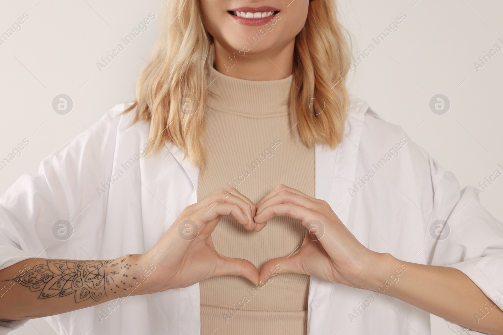 Photo of Happy volunteer making heart with her hands on light background, closeup