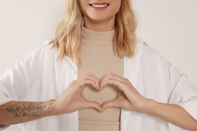 Photo of Happy volunteer making heart with her hands on light background, closeup