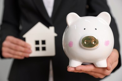 Photo of Woman holding house model against white background, focus on piggy bank