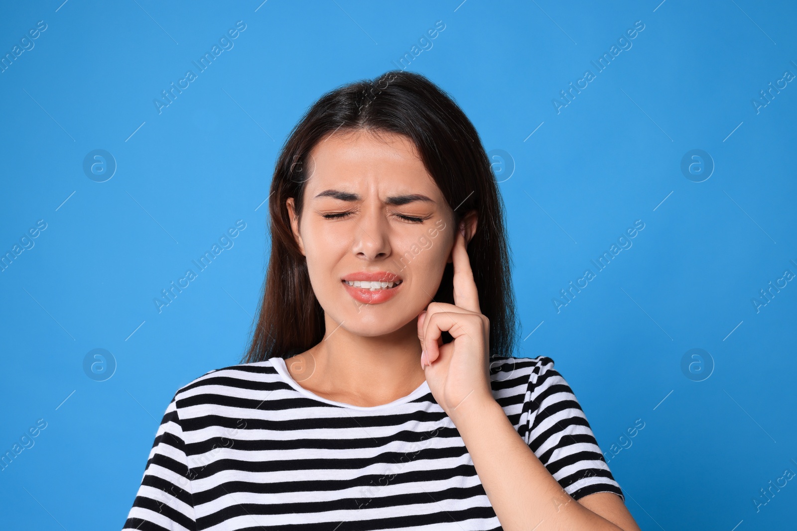 Photo of Young woman suffering from ear pain on light blue background