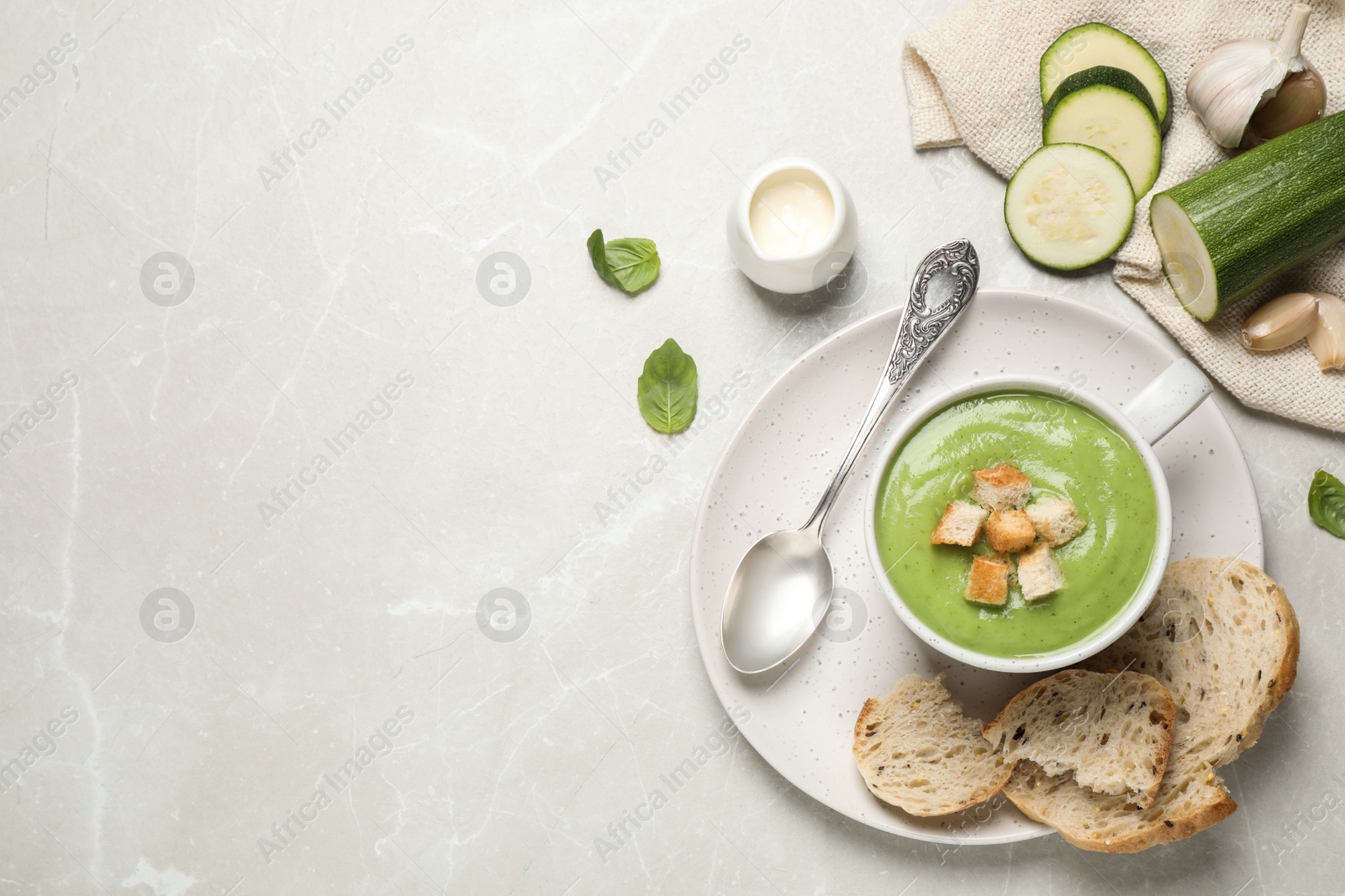 Photo of Tasty homemade zucchini cream soup served on light table, flat lay. Space for text