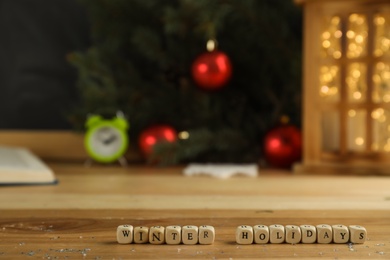 Wooden cubes with phrase Winter Holidays and blurred Christmas decor on background. Space for text