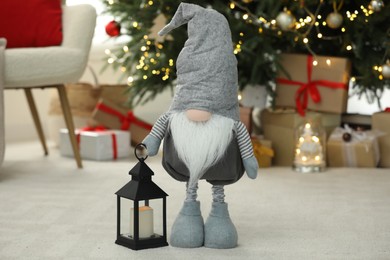 Photo of Funny Christmas gnome and lantern on floor in room with festive decoration
