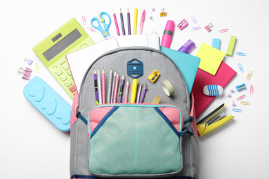 Stylish backpack with different school stationery on white background, top view