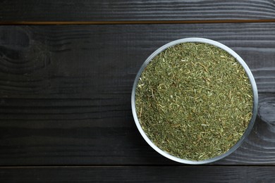Photo of Bowl with dried dill on black wooden table, top view. Space for text