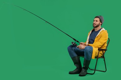 Fisherman with fishing rod on chair against green background, space for text