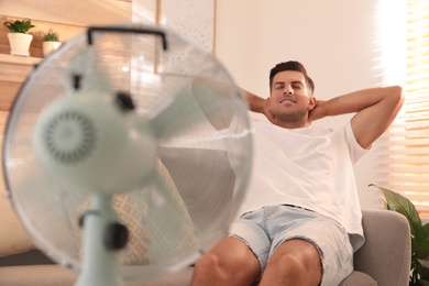 Man enjoying air flow from fan on sofa in living room. Summer heat