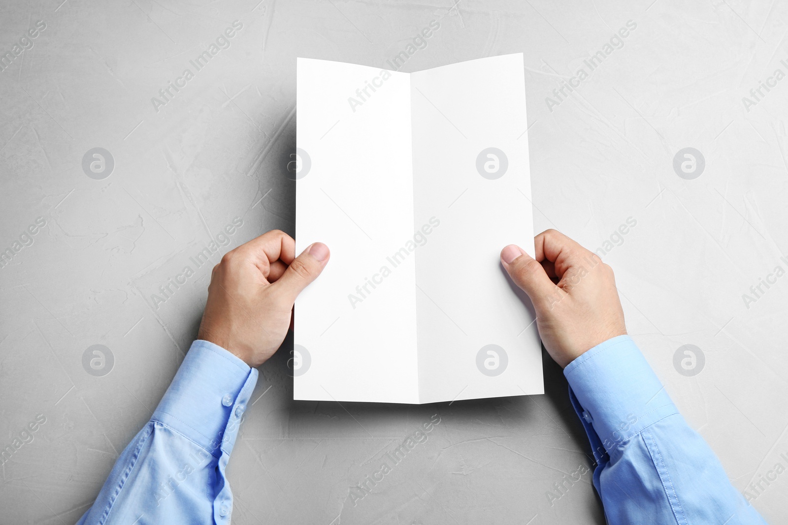 Photo of Young man holding blank brochure at grey table, top view. Mock up for design