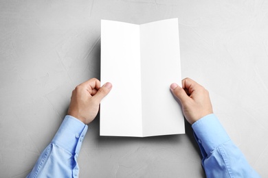 Young man holding blank brochure at grey table, top view. Mock up for design