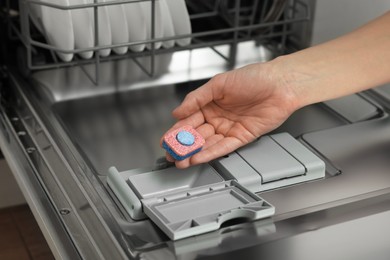 Photo of Woman putting detergent tablet into open dishwasher, closeup