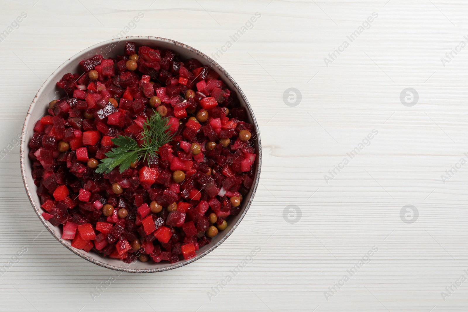 Photo of Bowl of delicious fresh vinaigrette salad on white wooden table, top view. Space for text